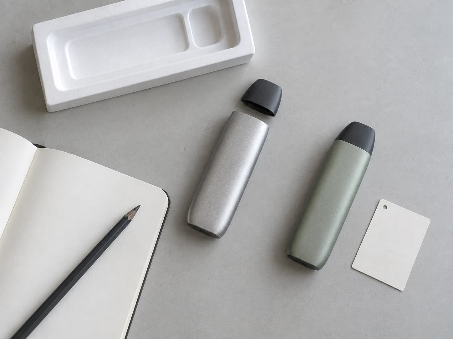 Concept still life of anonymous hardware exteriors beside a blank project notebook and packaging reference.